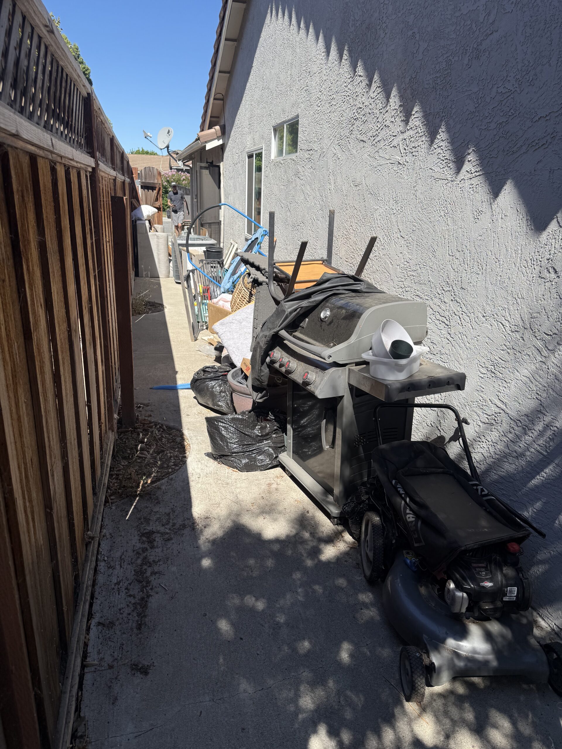 Residential yard with accumulated and trash bags staged for removal against building wall.