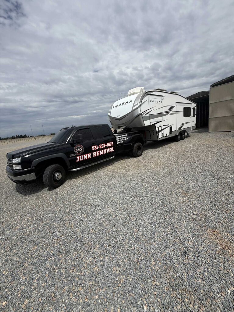 New state money for hauling off abandoned RVs starts January 1 10 MG branded truck towing white Cougar RV trailer on gravel, demonstrating RV hauling service