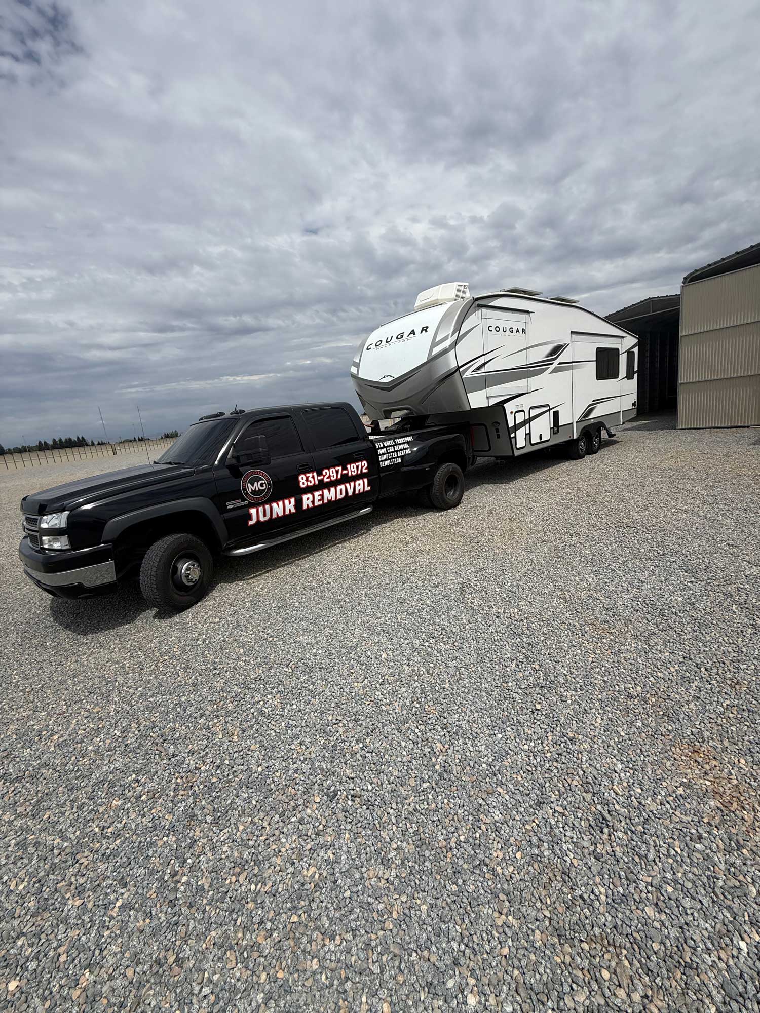 MG branded truck towing white Cougar RV trailer on gravel, demonstrating RV hauling service